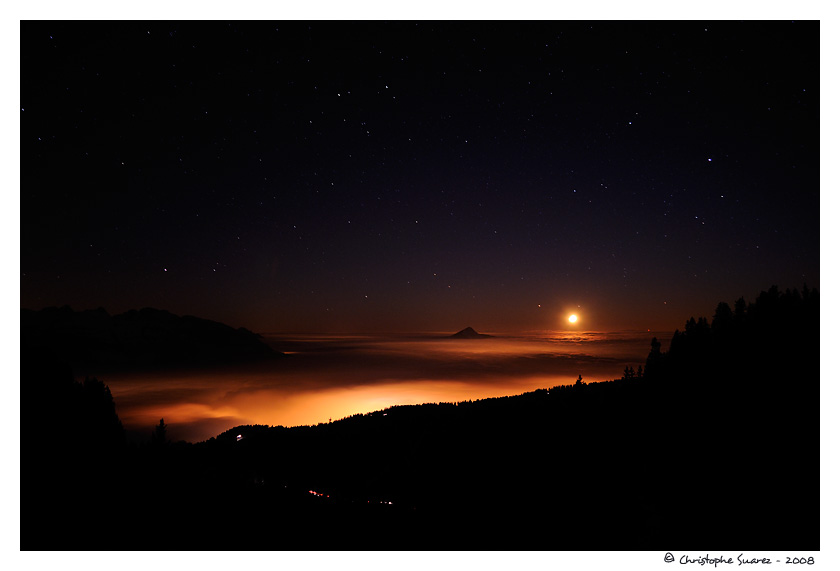 Paysage des Alpes la nuit - Mer de nuage claire par les lumires de Cluses et des Carroz sur la valle le L'Arve. En face, le Mle (1860m). La lune se couche.